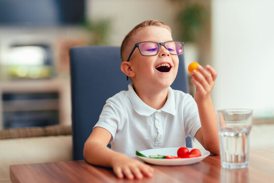 Cute boy in glasses eating vegetables at home