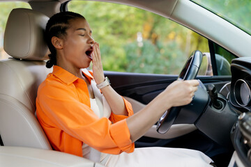 Yawning young black woman driving car and holding steering wheel. Sleepy african american female visibly tired, possibly after a long ride or early start, closeup