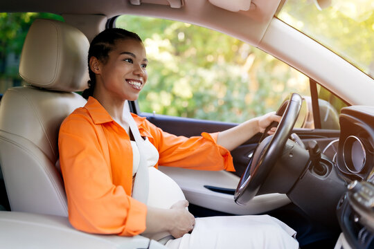 Happy black pregnant woman driving car in sunlight, smiling and enjoying the ride. Safe travel and joyful lifestyle during late pregnancy captured naturally, closeup