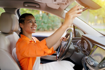African American woman adjusting rearview mirror before driving car. Young black female focused and smiling, showing readiness and responsibility, closeup
