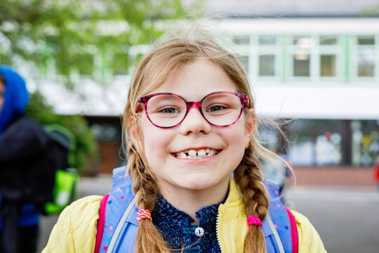 Little girl walking to school. Cute child with satchel and eyeglasses on school yard. Back to school. Happy school time.