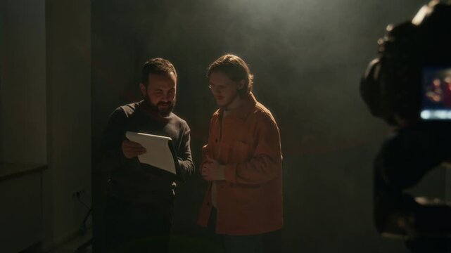 Filming director giving his advice and feedback to actor after filming his audition on camera in dimly lit studio