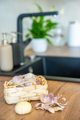 Basket with Chinese single clove garlic and one peeled garlic clove on kitchen countertop. Cooking preparation, fresh ingredient, and natural seasoning.