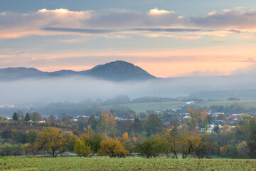 Scenic autumn landscape with misty hills and a charming village, evoking tranquility and natural...