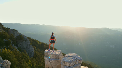 Determined runner triumphs on rocky peak, overlooking golden mountainous landscape. Captures...