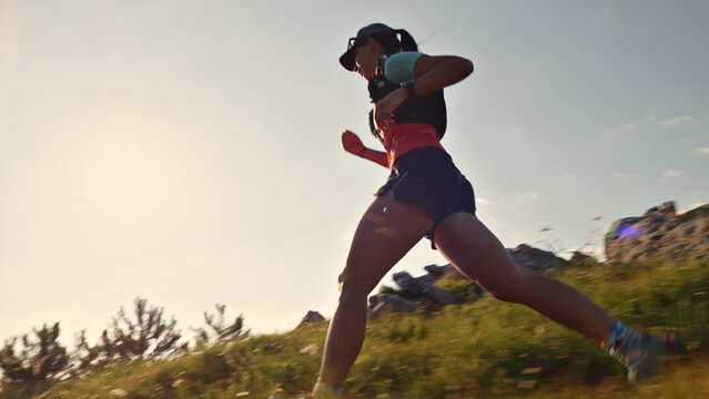 Determined female runner in athletic gear sprints across a grassy hillside, long exposure capturing sunset's warm glow, highlighting endurance, perseverance, and joy in cross-country running. - Powered by Adobe