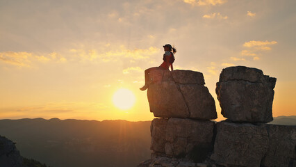 A woman triumphantly sits on a rocky peak at sunset, celebrating her cross-country running victory....