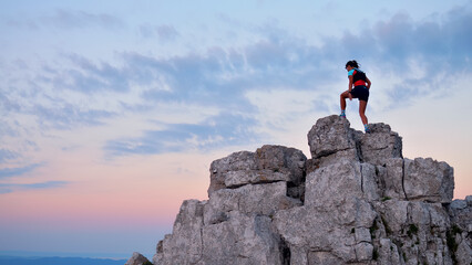 Determined runner triumphs atop rugged cliffs during serene sunset, embodying achievement and...