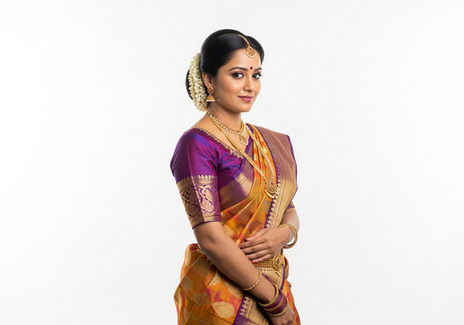 A young woman in a vibrant South Indian silk saree poses elegantly against a white backdrop.