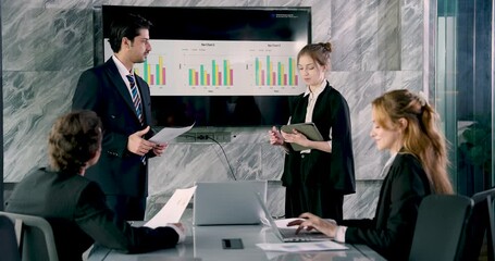 Asian businessman leading professional meeting while discussing bar chart data on screen with female colleague during collaborative business presentation in high-tech corporate office - Powered by Adobe