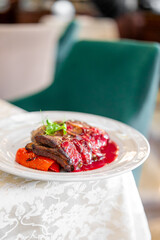 Close-up of glazed pork ribs served with roasted red peppers and greens on a white plate, gourmet dish in elegant setting, perfect for restaurant or culinary presentation.