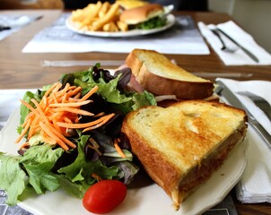 Ham and cheese toasted sandwich with salad in foreground with burger and chips in the background