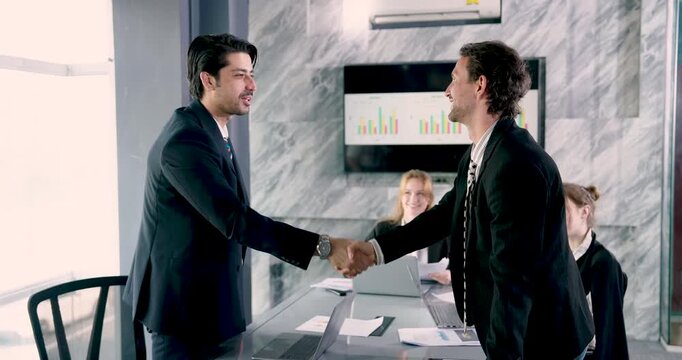 Two businessmen shaking hands after successful presentation, closing corporate deal with trust and agreement, businesswoman in background smiling, team acknowledging partnership progress