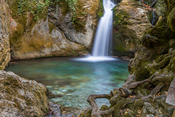 Close-up view of a vibrant turquoise pool and flowing waterfall surrounded by rocks and tree roots in Ayazma Nature Park, Bayramiç, Çanakkale, Turkey