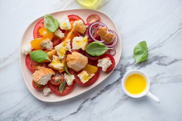 Beige plate with panzanella salad on a white stone background, horizontal shot, view from above