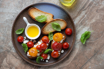Bruschettas with roasted mixed tomatoes, ricotta and basil, horizontal shot on a brown granite background, top view