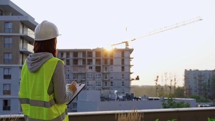 Fototapeta premium Construction female engineer taking notes and writing on clipboard while inspecting a building site