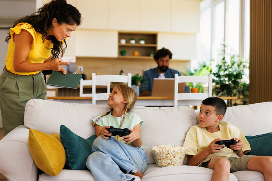 Mother scolding her two children playing video games while father is working from home