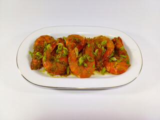 Serving of large, cooked prawns on a white oval platter with a gold rim. The prawns are bright orange-red, coated in a savory, textured sauce. Related to seafood cuisine, gourmet cooking, healthy eats