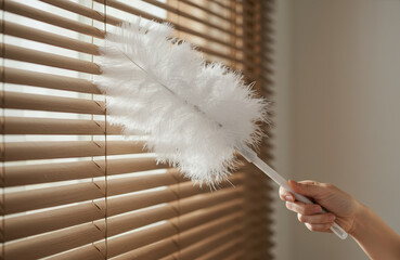 Close-up of a hand cleaning dusty blinds with a feather brush