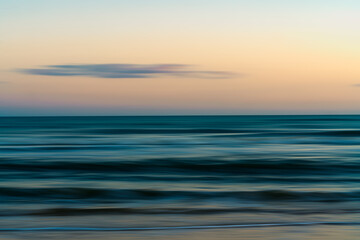 Fototapeta premium Calm ocean waves gently reaching the sandy shore under a soft pastel sky. Abstract