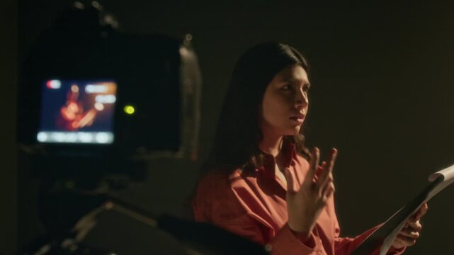 Young actress reading monologue off script while camera recording for her acting audition in dimly lit studio