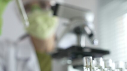 Close up of test tubes with a scientist analyzing plant samples in test tubes with a microscope in a laboratory at the background. Medicine, health care and science concept