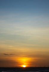 Sunset over ocean horizon with wind turbines silhouetted against warm golden and blue sky.