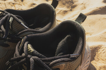 Pair of shoes with a black sole and a black strap. The shoes are on a sandy beach