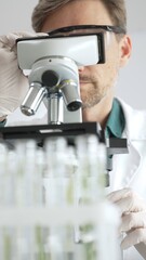 Scientific researcher in protective gear analyzing specimens through a microscope in a sterile laboratory environment. Medicine, healthcare and science concept