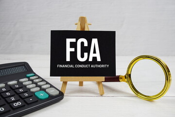 FCA abbreviation of Financial Conduct Authority text with magnifying glass and calculator on wooden...