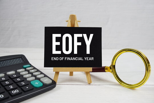 EOFY abbreviation of End of Financial Year text with magnifying glass and calculator on wooden background