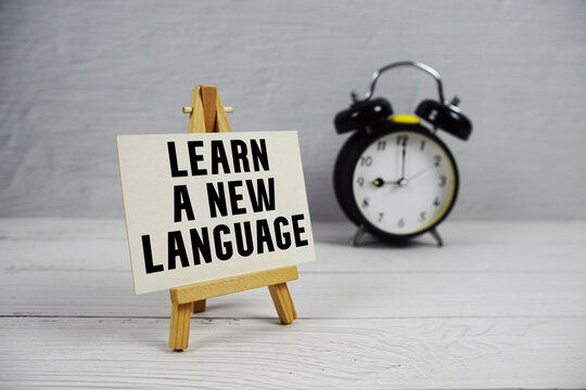 Learn A New Language text with easel and alarm clock on wooden background