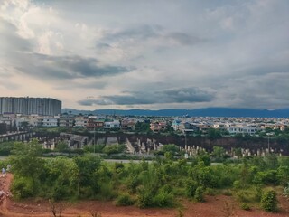Dramatic cityscape showing urban development, a high-rise building, and lush greenery under a moody, sunlit sky.