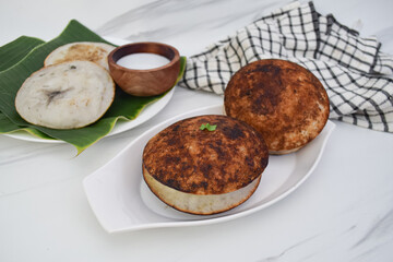 Stack of crispy, round, serabi typical Indonesian food, presented on a white plate. A small bowl of a white coconut milk.
