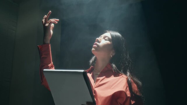 Low angle shot of young actress holding script and rehearsing dramatic scene for her acting auditions in dark studio