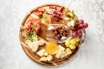 Charcuterie board with assorted cheeses, cured meats, nuts, grapes, dried fruits, and breadsticks on a white tablecloth, perfect for gourmet food photography and party settings.