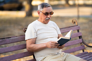 Fototapeta premium Senior man reading book on park bench