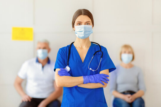 Portrait of young female doctor in uniform and face mask with patients waiting for coronavirus vaccination at clinic. Population immunization campaign, protection against covid-19 concept