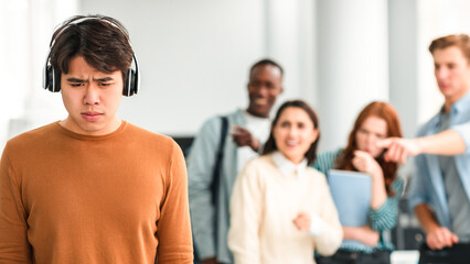 Bullying Concept. Rude diverse group of people mocking and making fun of sad asian guy wearing...