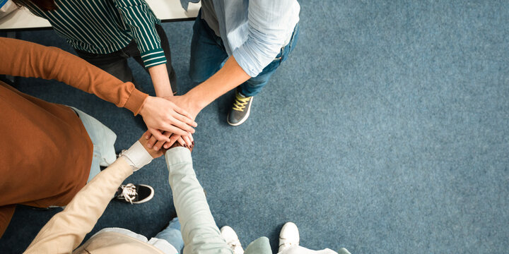 Teamwork And Unity Concept. Above top high angle view of young diverse group of people putting hands together standing in circle, celebrating collaboration and alliance. Panorama, banner, free space