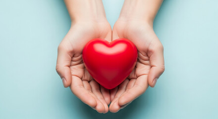 Obraz premium Two hands gently hold a red heart, symbolizing love, care, and Valentine's Day. Simple, clean background for text or branding