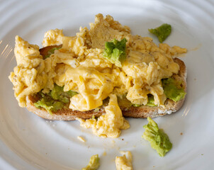 Scrambled eggs with avocado on toasted whole grain bread at a breakfast table