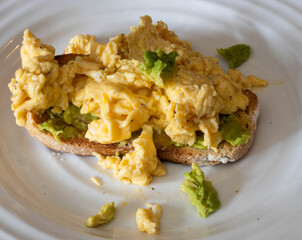 Scrambled eggs with avocado on toasted whole grain bread at a breakfast table
