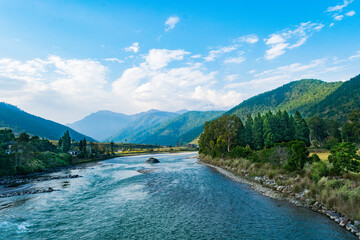 Peaceful river flowing through the Punakha valley in Bhutan, surrounded by green mountains and blue sky.