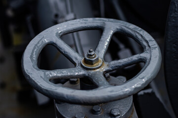 Detailed view of a gray-painted metal valve wheel in an industrial setting, showing texture, wear, and mechanical components.