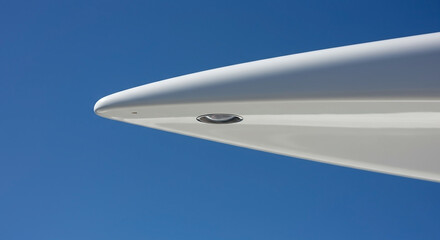 Minimalist abstract view of a sleek white sailboat masthead tip with a small light against a clear blue summer sky.