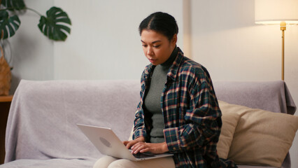 Hispanic woman type on laptop keyboard sitting on sofa