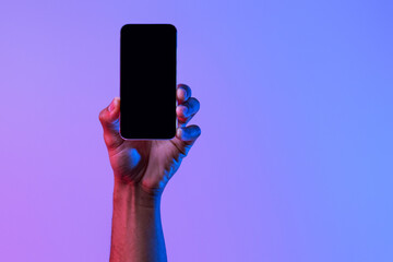 Social network and modern technology. Female hand holds phone with blank screen on neon background, close up, copy space