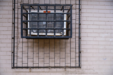 Air conditioning unit mounted on a brick wall, enclosed in a protective metal cage for safety and security.